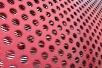 A texture of holes in red painted iron. It's a macro of a red dustbin