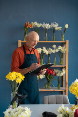 Light-skinned elderly man florist carefully draws up paperwork