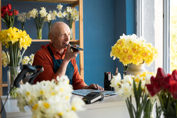 An elderly man with pleasant appearance, florist, is holding phone in his hands and talking.