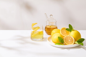 A round dish of fresh lemon placed next a honey jar and a glass of lemon juice on the right side of photo. The left side is blank for presentation or adding text