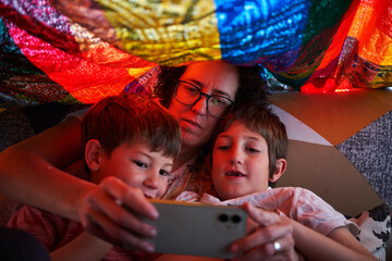 Mother and her children watching the smart phone under a blanket