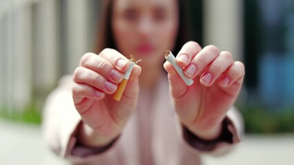 Focused on hands of serious female crushing cigarette outdoors. Confident caucasian female showing significant and positive health choice. Blurred background. Concept of smoking and dependence.