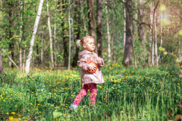 A little girl of 2-3 years old stays in the forest and enjoys nature. Background of a green forest. She is joyful and dreamy.