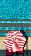 Vibrant red and white striped umbrella by shimmering turquoise pool captures essence of relaxation...