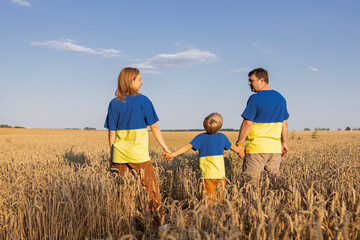Ukrainian family in identical yellow and blue T-shirts stands among ears of wheat in field. Stop...