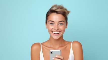 Radiant young woman with blonde hair, smiling joyously while holding a smartphone against a soft blue background