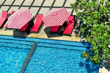 Red and white striped umbrellas next to matching loungers by a vibrant blue pool epitomize the...