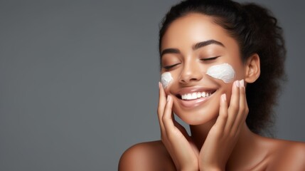 Beautiful young woman applying facial cream, her smile expressing pleasure and care for skin health