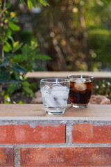 Front view of 2 glasses filled with water and soft drink with ice, on a wallflower on an outdoor...
