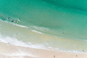 drone overhead aerial view of the shore of a beach with people walking and learning to surf.