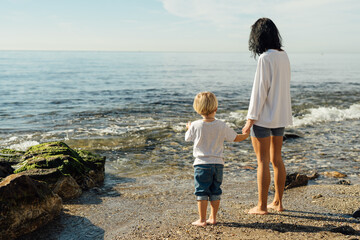 young mother and son stand on the seashore. A woman with a child stands on the beach, rest and travel with children, vacation on the sea. family on vacation at sea.