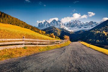 Sunny autumn view of asphalt road in Santa Maddalena village with Geisler or Odle Dolomites Group peaks on background. Colorful morning scene of Dolomite Alps, Italy, Europe.