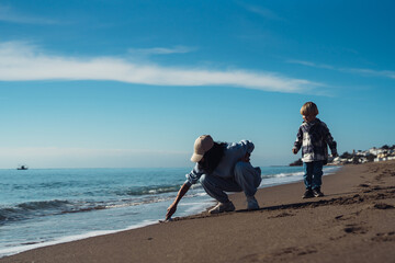 A young mother and her three-year-old child are playing on the sand near the sea. Family idyll. Holidays by the sea.