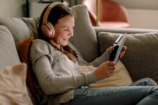 Happy teenage girl on sofa watching movie through digital tablet at home