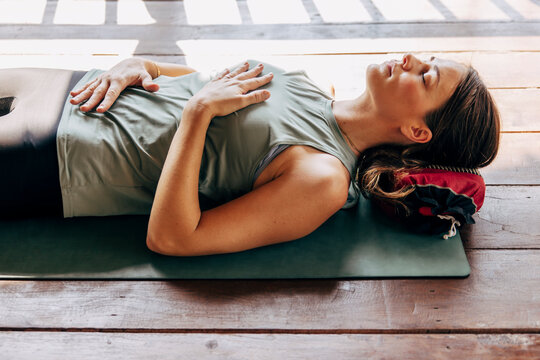Mature woman with hands on chest and stomach lying down on yoga mat at wellness resort