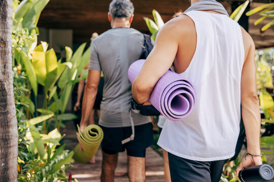 Rear view of men holding rolled up yoga mats while walking towards resort