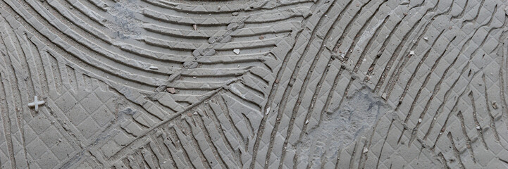 Panoramic image. Background of old grey tile adhesive on the floor. Abstract pattern of notched...