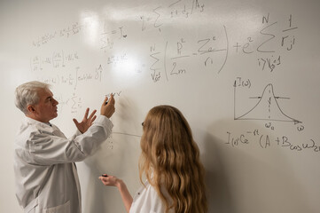 An elderly man and a young woman at a white board. Colleagues scientists discuss work issues. 
