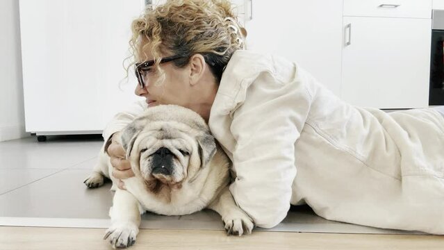 One happy woman dog owner doing cuddles at her old pet pug at home laying on the floor enjoying bst friend canine animal love and pet therapy alone having fun. People domestic lifestyle dog playing