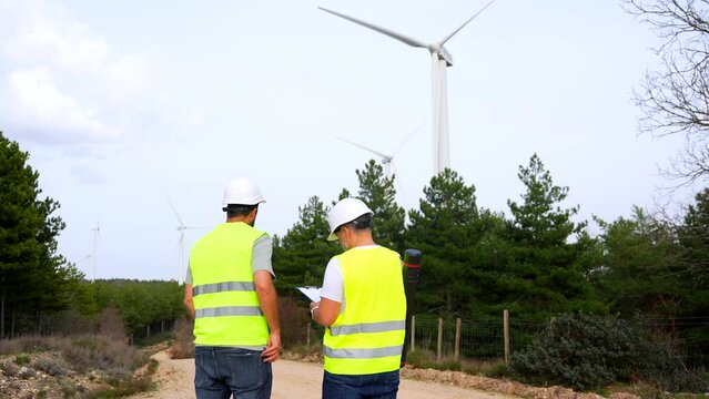 Technicians inspecting wind turbines in a green energy park talking to the mobile and taking notes