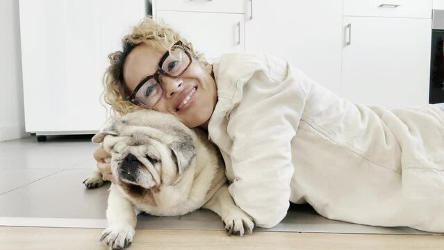 One happy woman dog owner doing cuddles at her old pet pug at home laying on the floor enjoying bst friend canine animal love and pet therapy alone having fun. People domestic lifestyle dog playing