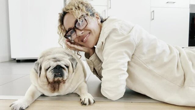 One adult woman alone at home relaxing on the floor with her best friend dog enjoying cuddle and fun with old pug companion. Animal canine relationship domestic real lifestyle female people