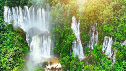 A hidden gem in the heart of a lush tropical rainforest, this colossal waterfall cascades gracefully through the dense emerald canopy. Lush Wild Woods: Earth's Green Jewel. Drone view. Thailand. 