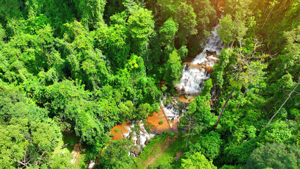 Nature's masterpiece unveiled - an enchanting waterfall concealed within a tranquil rainforest, unveiled by drone, flows gently down layered rocks, serenading the lush, verdant wilderness. Thailand.
