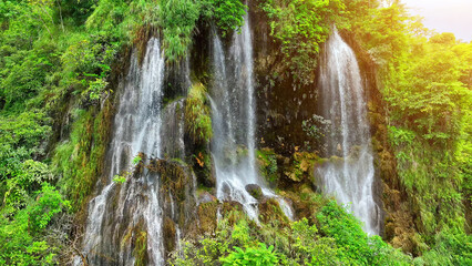 Enchanting Aerial View: A hidden gem, a magical waterfall nestled in the heart of a lush tropical rainforest, its emerald waters glistening under the dappled sunlight, captured from above by a drone.
