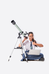 Isolated little Indian asian schoolgirl in school uniform looking into a telescope.