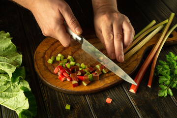 Preparing a vegetarian dish from rheum plant. Chef hands use a knife to slicing rhubarb stalks on a...