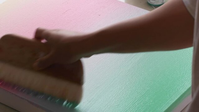 A diverse biracial female artist, paints a smooth pastel gradient with a wide brush using back and forth motion