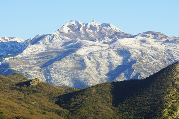 View of snow-capped Mount Lovcen against a blue sky and a fragment of forested Mount Vrmac below -...