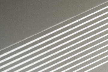 白い壁に日差しがつくるブラインドの縞模様の光と影