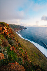 View of rough ocean with waves, volcanic beach, sunset over a huge cliff  in Lighthouse Ponta do Pargo, Madeira, Portugal