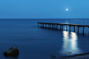 Moonlit Serenity: Nighttime Pier with Moonlight Reflecting on the Calm Sea Surface, Blurred Foreground Ripples Enhancing the Peaceful Night Atmosphere