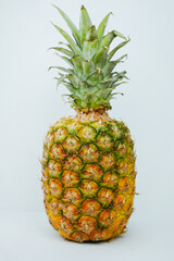 Fototapeta premium A ripe pineapple with a green crown on a white background, highlighting its textured yellow and green skin, perfect for culinary and health visuals