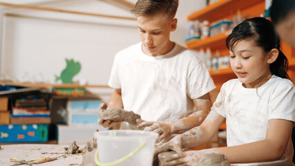 Caucasian boy modeling bowl of clay while cute asian girl working on dough at pottery workshop....