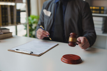 Young lawyer or legal advisor holding the gavel of justice on the table with contract documents and business agreements. Signing a legal contract Law firm justice concept.