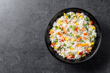 White rice with vegetables in a black bowl on black background. Top view. Copy space