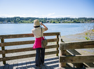 Woman taking photos using a smartphone on the bridge in Poulsbo. Poulsbo is a city on Liberty Bay in Kitsap County, Washington State.