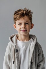 A young boy dressed in a casual long-sleeve top and comfy pants stands with arms crossed, against a dark grey backdrop, conveying a sense of youthful confidence