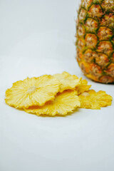 Crisp, dried pineapple slices lay in focus, with their source fruit softly blurred behind them, emphasizing natural sweetness