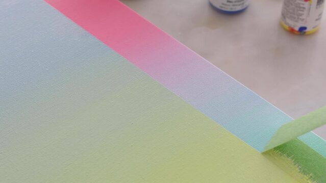 An artist pulls masking tape, to reveal a crisp hard edge gradient painted artist canvas.
