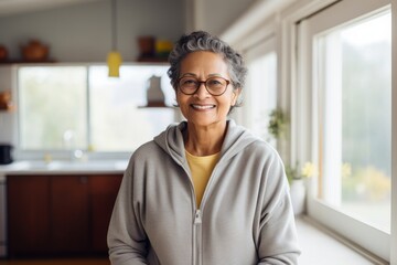 Portrait of a happy indian woman in her 80s wearing a zip-up fleece hoodie while standing against modern minimalist interior