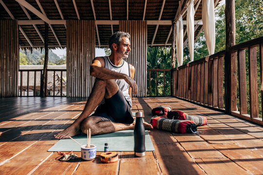 Mature man doing Matsyendrasana pose on yoga mat at wellness resort