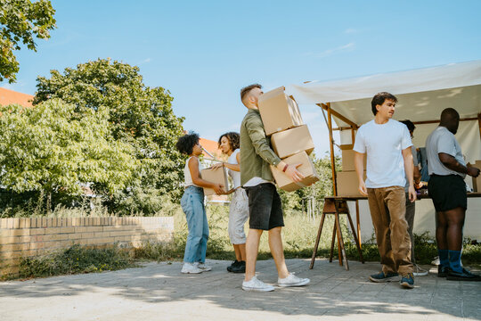 Side view of male volunteer holding stack of cardboard boxes and walking at community center