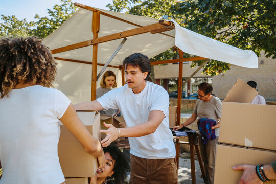 Male volunteer helping female colleagues while holding cardboard boxes during charity drive at community center