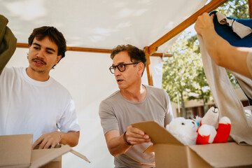 Young volunteer discussing with senior male colleague while sorting clothes and stuffed toys in boxes at community cente