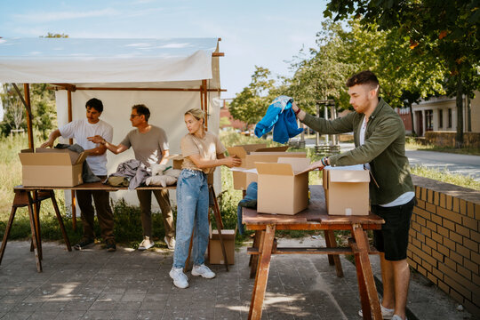 Group of male and female volunteers sorting clothes from cardboard boxes on table at community center